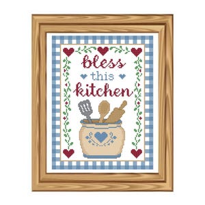 May include: Framed cross-stitch art with a kitchen theme. The artwork features the words "bless this kitchen" in red script, with a blue and white gingham border. A beige jar with kitchen utensils is in the centre.