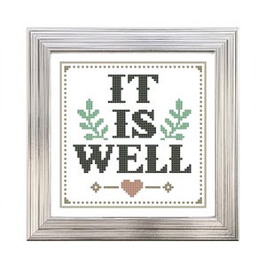 May include: A framed cross-stitch artwork with the words "IT IS WELL" in black, green, and pink. The artwork is in a white frame with a silver finish. The design includes floral elements and a heart.