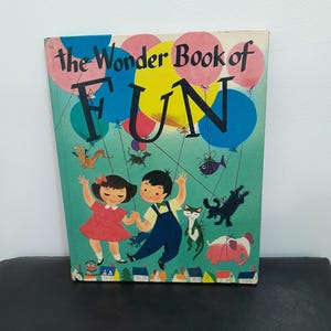 May include: Vintage children's book titled "The Wonder Book of FUN." The cover features illustrations of two children, balloons, and various animals. The background is a teal color with a row of houses at the bottom.
