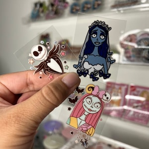 May include: Clear stickers featuring characters from The Nightmare Before Christmas. Includes Jack Skellington in black and white, the Corpse Bride in blue, and Sally in pink and yellow. Decorative stars and bats are also included.