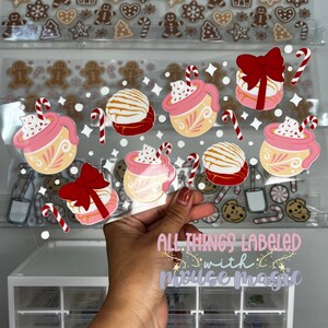May include: A sheet of clear vinyl stickers featuring a variety of winter-themed designs. The stickers include mugs of hot chocolate with whipped cream and candy canes, along with gingerbread cookies and other festive treats. The text "All Things Labeled with Mouse Magic" is printed at the bottom of the sheet.