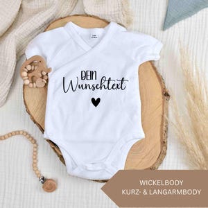 Könnte beinhalten: Ein weißer Kurzarm-Wickelbody für Babys mit Druckknopfverschluss. Auf der Brust befindet sich der schwarze Schriftzug 'DEIN Wunschtext' über einem kleinen schwarzen Herzsymbol. Das Kleidungsstück hat ein Etikett mit der Größe 0-3 Monate.