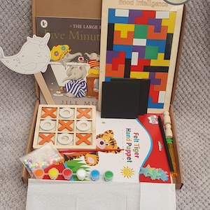 May include: A box filled with various children's toys and activities, including a wooden noughts and crosses game, a felt tiger hand puppet, a book titled "Five Minute Stories", a wooden puzzle, and paint supplies.