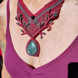Op de afbeelding: Een rode en grijze macramé ketting met een grote, traanvormige, blauwgroene edelsteen hanger.