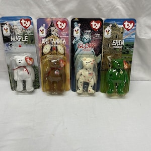 May include: Four Ty Beanie Babies in their original packaging. The bears are Maple, Britannia, Glory, and Erin. Each bear is wearing a different outfit and has a different background image on the packaging.