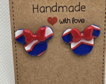 Puede incluir: Un par de pendientes hechos a mano con forma de cabeza de ratón con un lazo rojo. Los pendientes son azules, blancos y rojos. Se presentan en una tarjeta marrón con las palabras "Handmade with love".