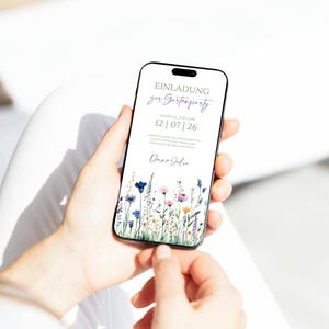 May include: A digital invitation on a smartphone screen for a garden party. The invitation features a floral design with blue, pink, and yellow flowers. The text on the invitation reads "Einladung zur Gartenparty Samstag den 12.07.26  Dana & Julia".