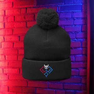 May include: Black beanie hat with a pom-pom. The turned-up cuff displays a geometric design with a skull emblem. The background is a brick wall lit with red and blue neon lights.