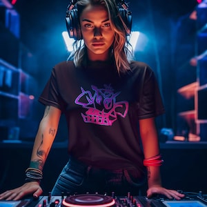 Può includere: Una donna indossa una maglietta nera con un design grafico rosa e viola e si trova davanti a un mixer DJ. Indossa delle cuffie e ha un'espressione seria sul viso.