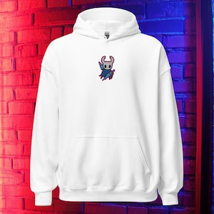 Pode incluir: Moletom branco com capuz, bolso frontal e capuz. O moletom apresenta um desenho bordado de um personagem em azul, vermelho e branco. O desenho está localizado na parte superior esquerda do peito. O moletom é feito de um material macio.