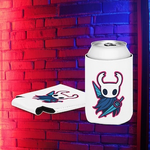 Puede incluir: Enfriador de latas blanco con un diseño de personaje de dibujos animados. El diseño presenta un personaje blanco con una cara negra, una cabeza curva y una capa azul. También se ve un segundo enfriador con el mismo diseño.