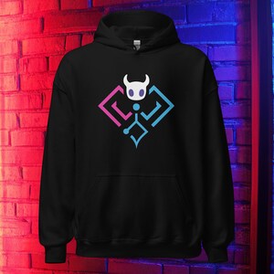 May include: Black hooded sweatshirt with a white horned character design inside a pink and blue geometric shape. The design is on the front. The sweatshirt has a drawstring hood and a kangaroo pocket.