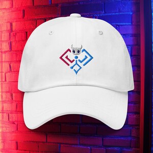 Puede incluir: Gorra de béisbol blanca con visera curva. La gorra presenta un diseño bordado de un personaje estilizado en rojo y azul. El diseño está centrado en la parte delantera. La gorra está hecha de un material suave.