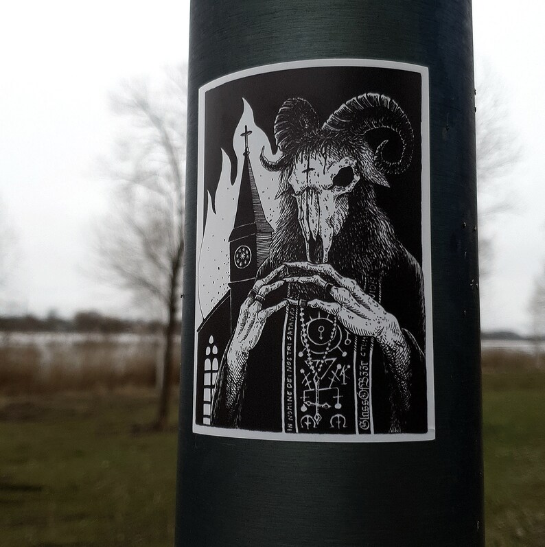 May include: Black and white sticker of a horned demon with a skull-like face, holding a book with the text "IN NOMINE DEI NOSTRI SATANAI" and "Gnosis Occult" in a gothic font. The demon is standing in front of a church with flames behind it.
