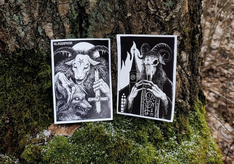 May include: Two black and white stickers featuring a goat-like demon with horns and a cross. The first sticker shows the demon holding a cross and a wolf. The second sticker shows the demon wearing a robe and holding a rosary in front of a church.
