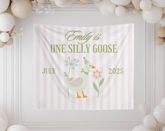 May include: A party backdrop with a pink and white striped pattern. The banner reads "Emily is ONE SILLY GOOSE" with a cartoon goose illustration. The backdrop is decorated with balloons in white and beige.