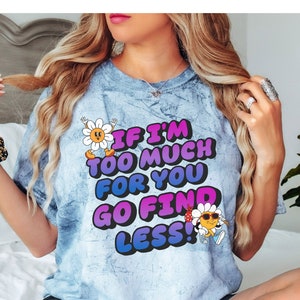 May include: A light blue tie-dye t-shirt with a cartoon flower and sun graphic. The shirt has the text "If I'm Too Much For You Go Find Less!" printed on it.