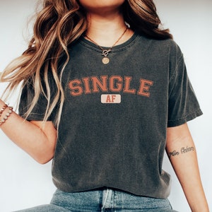 May include: A dark gray t-shirt with the text "SINGLE AF" in a red and orange collegiate-style font.