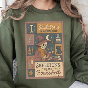 May include: Green sweatshirt with a graphic that reads "Skeletons in my Bookshelf." The graphic features a skeleton wearing a witch hat, reading a book, with a black cat, potion bottles, and a crescent moon.