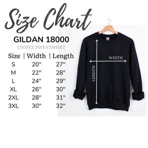 May include: A black Gildan 18000 unisex sweatshirt hangs on a wooden hanger. A size chart shows measurements in inches for sizes S through 3XL. The chart includes width and length measurements for each size.