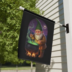 May include: A black rectangular garden flag featuring a gnome with a long white beard and a green hat. The gnome is stirring a black cauldron over a fire, with green smoke rising from the pot. The background shows a night sky with a moon and bats.