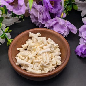 May include: A brown wooden bowl filled with white bone-shaped dog treats. The bowl is sitting on a dark gray surface.