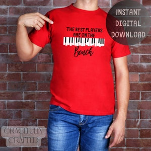 May include: Red t-shirt with a white graphic that says "The best players are on the bench" with a black piano keyboard graphic above the text.