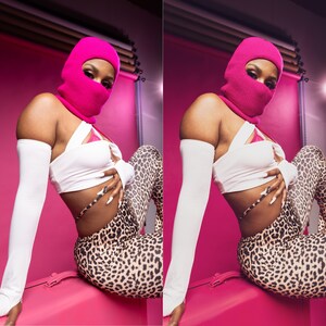 Op de afbeelding: Een persoon draagt een felroze bivakmuts, een witte crop top en een legging met luipaardprint. De persoon draagt ook witte armmouwen. De achtergrond is felroze.