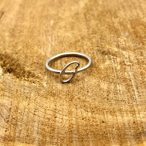 May include: A silver ring featuring the letter "G" in a cursive script.