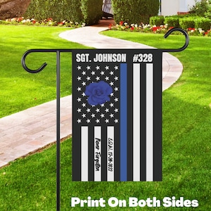 May include: A black and white American flag with a blue line and a blue rose. The flag has the text "Sgt. Johnson #328" and "EOW 12-14-2022 Never Forgotten" printed on it. The flag is printed on both sides.