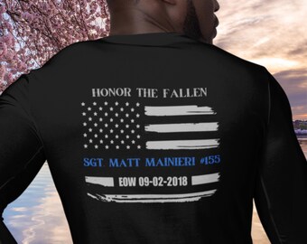 May include: Black long-sleeve shirt with a blue and white American flag design. The text "HONOR THE FALLEN" is above the flag. Below the flag is the text "SGT. MATT MAINIERI #155" and "EOW 09-02-2018".