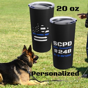 May include: A black 20 oz. stainless steel tumbler with a blue line and American flag paw print design. The tumbler is personalized with the text "SCPD OFC. Demarco #248 K-9 Bruno".