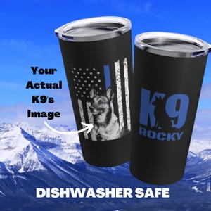 May include: A black stainless steel tumbler with a blue and white American flag design. The flag has a blue stripe down the middle. A German Shepherd dog is pictured on the flag. The tumbler has a silver lid and the text "K9 ROCKY" is printed on the other side.