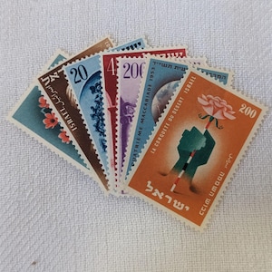 May include: A collection of vintage Israeli postage stamps featuring various designs, including a globe, a building, and a hand holding a flower. The stamps are in different colors, including blue, red, orange, and green. The text on the stamps includes "Israel", "La Conquete du Desert Israel", and "Quatrième Maccabiade 1953".