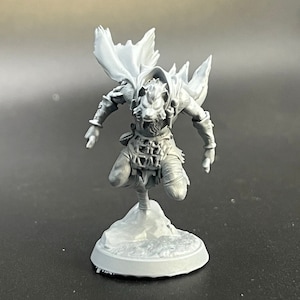 Pode incluir: Uma miniatura cinza impressa em 3D de uma figura humanoide com cabeça de lobo usando uma capa e segurando uma adaga. A figura está em pé sobre uma base redonda.