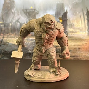 May include: A detailed miniature figurine of a large, armored, and angry-looking orc holding a hammer. The orc is painted in a brown and grey color scheme and is standing on a circular base.