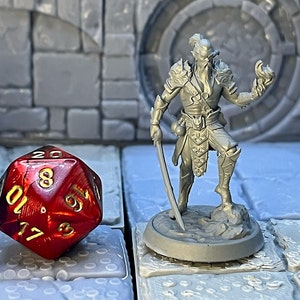 Könnte beinhalten: Eine graue Plastik-Miniaturfigur eines humanoiden Wesens mit Bart und Schwert. Die Figur steht auf einem grauen Plastiksockel mit strukturierter Oberfläche. Die Figur hält ein Schwert in der einen Hand und einen Feuereffekt in der anderen. Ein roter 20-seitiger Würfel mit goldenen Zahlen befindet sich im Vordergrund.
