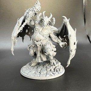 May include: A gray, detailed miniature of a demon with wings, holding a torch in one hand. The demon is standing on a circular base with a textured surface.