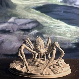 May include: A grey, detailed miniature of a spider with eight legs, standing on a round base. The spider is facing forward with its legs spread out.