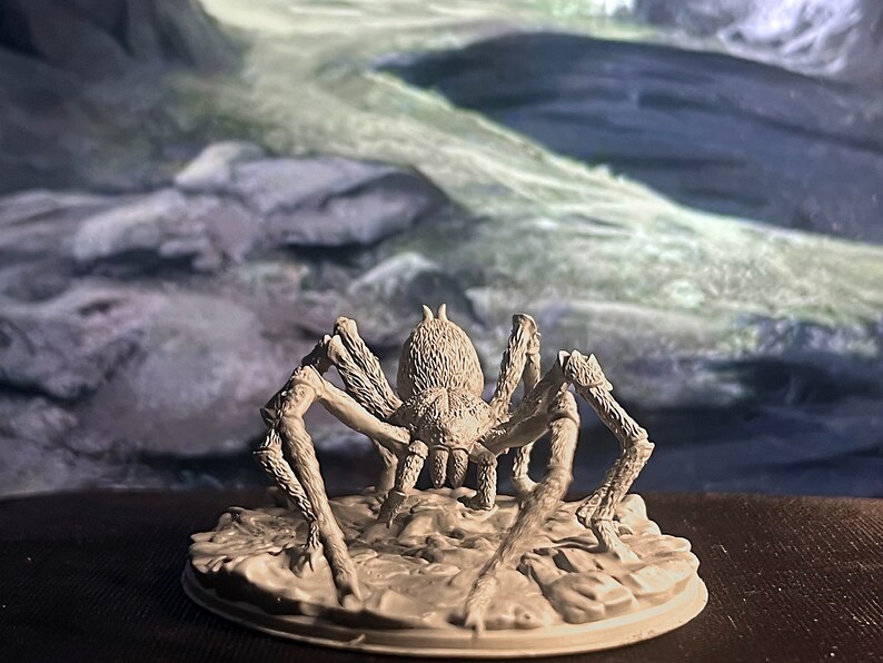 May include: A grey, detailed miniature of a spider with eight legs, standing on a round base. The spider is facing forward with its legs spread out.