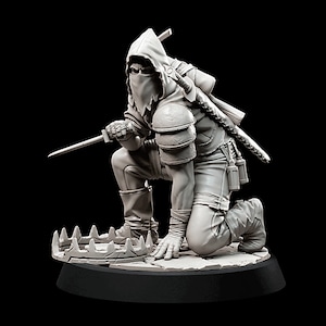 Pode incluir: Uma figura cinza, encapuzada e mascarada, ajoelhada em uma base com uma armadilha de metal. A figura segura uma adaga em uma mão e tem uma espada presa nas costas.