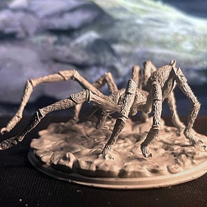 May include: A grey, detailed, plastic miniature of a spider with eight legs. The spider is posed on a grey, textured base.