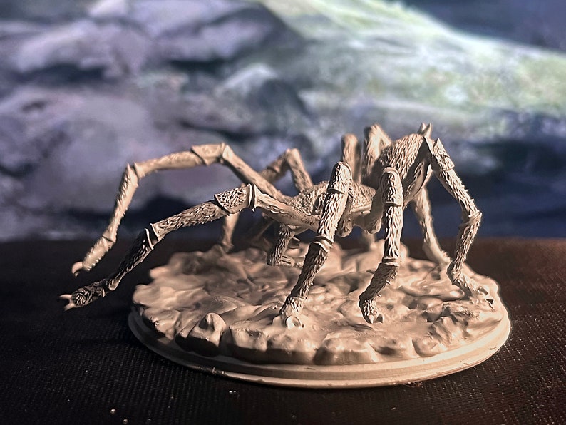 May include: A grey, detailed, plastic miniature of a spider with eight legs. The spider is posed on a grey, textured base.