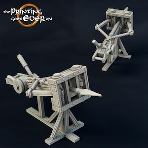 May include: A 3D printed model of a medieval siege weapon, a trebuchet, with a wooden frame and metal accents. The trebuchet is in a cocked position, ready to launch a projectile.