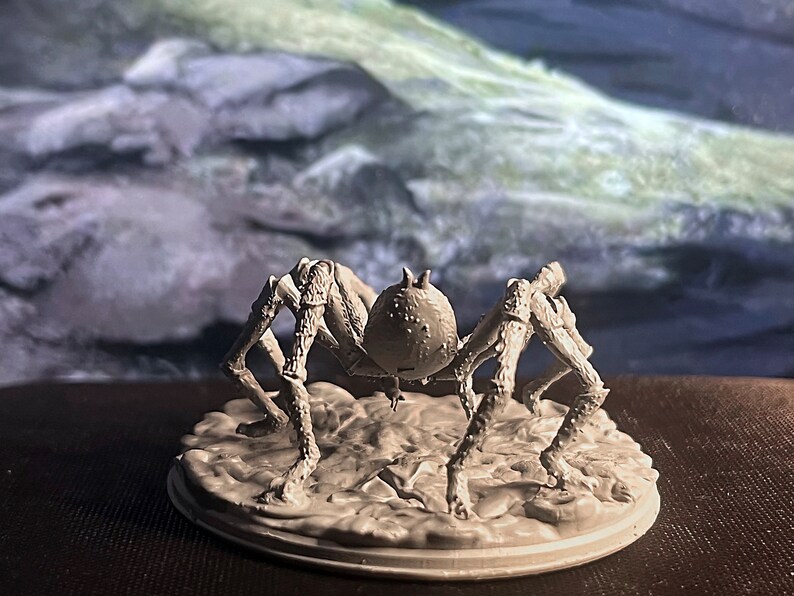 May include: A white, detailed, plastic miniature of a spider with eight legs and a round body. The spider is standing on a round, white base.