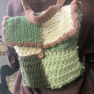 May include: A handmade crochet backpack in shades of green, cream, and brown. The bag has a patchwork design, a button closure, and a scalloped edge. The straps are also crocheted.