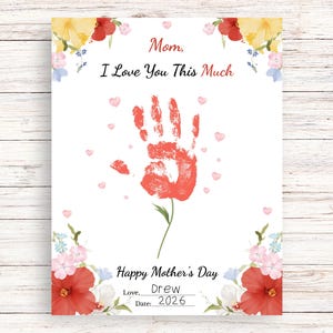 Può includere: Un biglietto bianco per la festa della mamma con un'impronta di mano rossa al centro, circondata da piccoli cuori rosa. Il testo recita "Mamma, ti voglio bene così tanto" e "Buona festa della mamma". Accenti floreali in rosso, giallo e rosa decorano i bordi. Firmato "Drew, 2026."