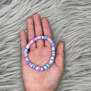 May include: A colorful bracelet made of small, round, flat beads in pink, blue, and white. The bracelet is arranged in a circular pattern.