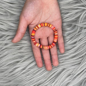 May include: A colorful bracelet made of stacked, round, plastic beads in shades of orange, red, and white.