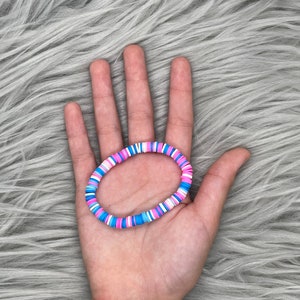 May include: A colorful beaded bracelet with pink, blue, and white beads. The bracelet is made of small, round beads that are strung together on a stretchy cord.